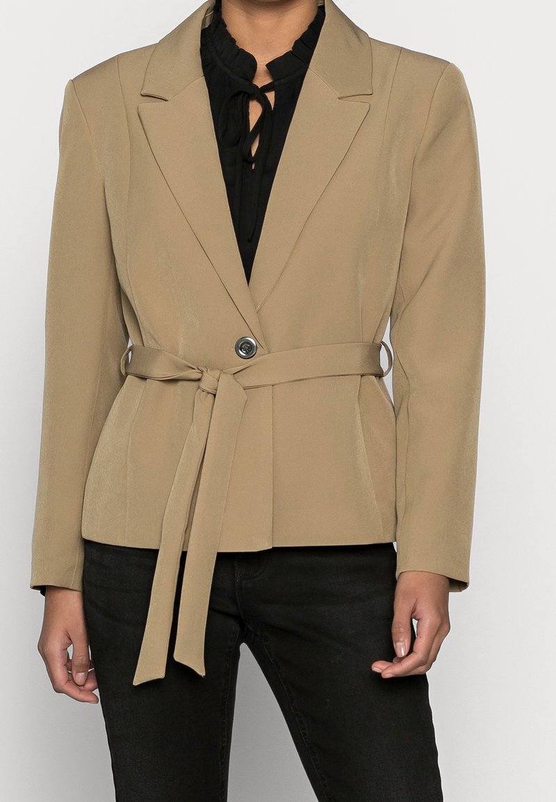 Beige blazer se šitým střihem, s jedním knoflíkem, s páskem na zavázání v pase a klopami. Texturovaná látka.