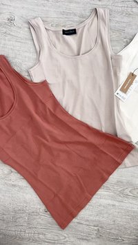 Três camisetas sem mangas em terracota, bege e branco. Feitas de tecido macio, com decotes redondos, texturas suaves e sem padrões visíveis.