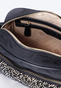 Bolso de tela acolchada negra con cremalleras doradas, que cuenta con un interior beige. La sección inferior tiene un patrón texturizado en blanco y negro.