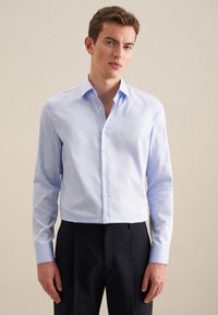 Jasnoniebieska koszula zapinana na guziki z wyraźnym kołnierzykiem, długimi rękawami i dopasowanym krojem. Gładka faktura i delikatny blask. Połączona z ciemnymi spodniami.