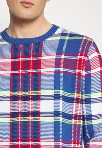 Stickad tröja med ett flerfärgat rutig mönster i blått, rött och vitt med detaljer i gult och grönt, rundad halsringning och texturerad tyg.