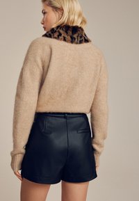 Pull beige en tricot avec un col en fourrure imprimé léopard, assorti à un short en similicuir noir, présentant une texture lisse et une coupe ajustée.