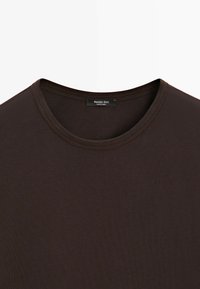 T-shirt marron foncé col rond avec une étiquette de marque Massimo Dutti visible cousue à l'intérieur du col.