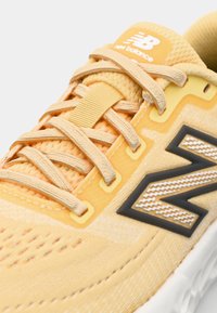 Yellow athletic shoe with breathable fabric, textured laces, and a black-and-white logo. Features cushioned sole and reinforced stitching.