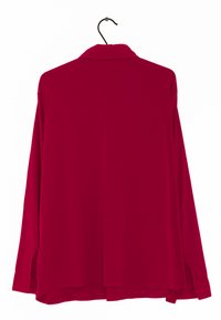 Rotes Langarmhemd mit Kragen, aus glattem Stoff. Hat einen geraden Schnitt, seitliche Schlitze und geknöpfte Manschetten. Hängt an einem schwarzen Haken.