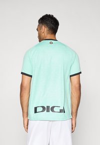 Mann in einem hellgrünen Sporttrikot mit schwarzem Kragen und Saum, mit dem Text "DIGI" auf dem unteren Rücken und einem kleinen Emblem auf dem oberen Rücken.