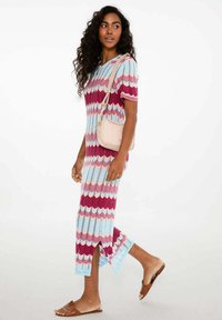 Maxi sukienka z falowanym wzorem w kolorze niebieskim, różowym i bordowym. Wykonana z prążkowanej dzianiny, z krótkimi rękawami i bocznymi rozporkami; zestawiona z beżową torebką.