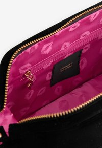 Borsetta in suede nera con cerniera dorata. L'interno presenta una fodera rosa con un motivo di impronte di labbra e una tasca interna con zip e linguetta.
