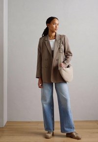 Dobbeltræsser beige blazer over en hvid top, parret med lyseblå vide jeans og en blød, buet beige skuldertaske.