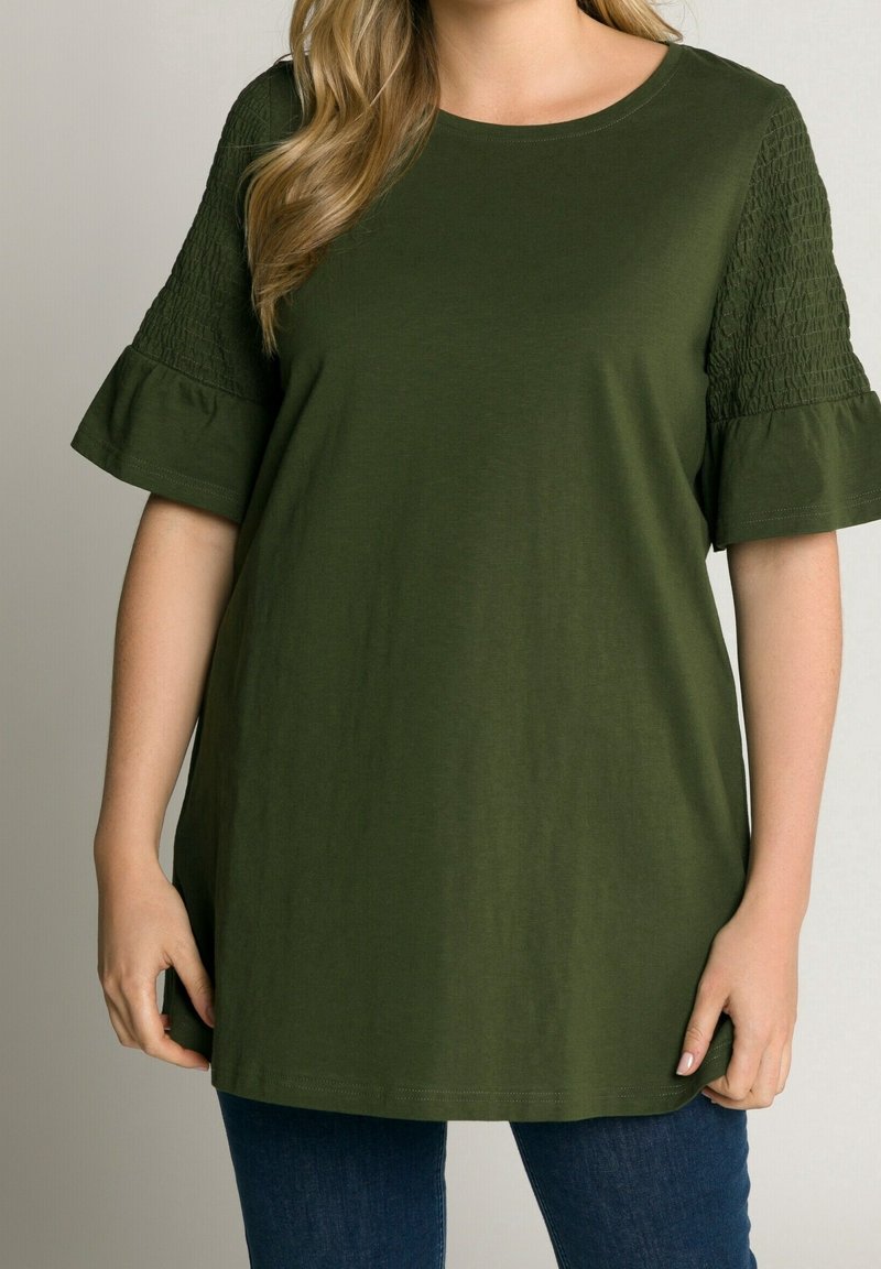 Olivgrön topp med korta volangärmar som har smockdetaljer. Mjuk tyg, avslappnad passform, rund halsringning och något längre längd.