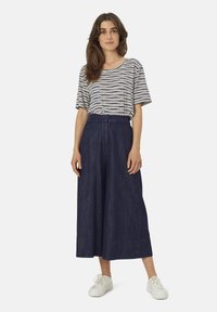 Camisa de manga corta a rayas con escote redondo, combinada con culottes de mezclilla oscuros de pierna ancha y zapatillas blancas, mostrando un ajuste holgado.