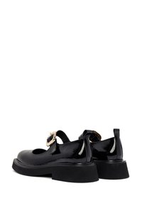 Scarpe in vernice nera con punta arrotondata, cinturino alla caviglia e fibbia dorata. Presentano una suola nera spessa per un'altezza maggiore.