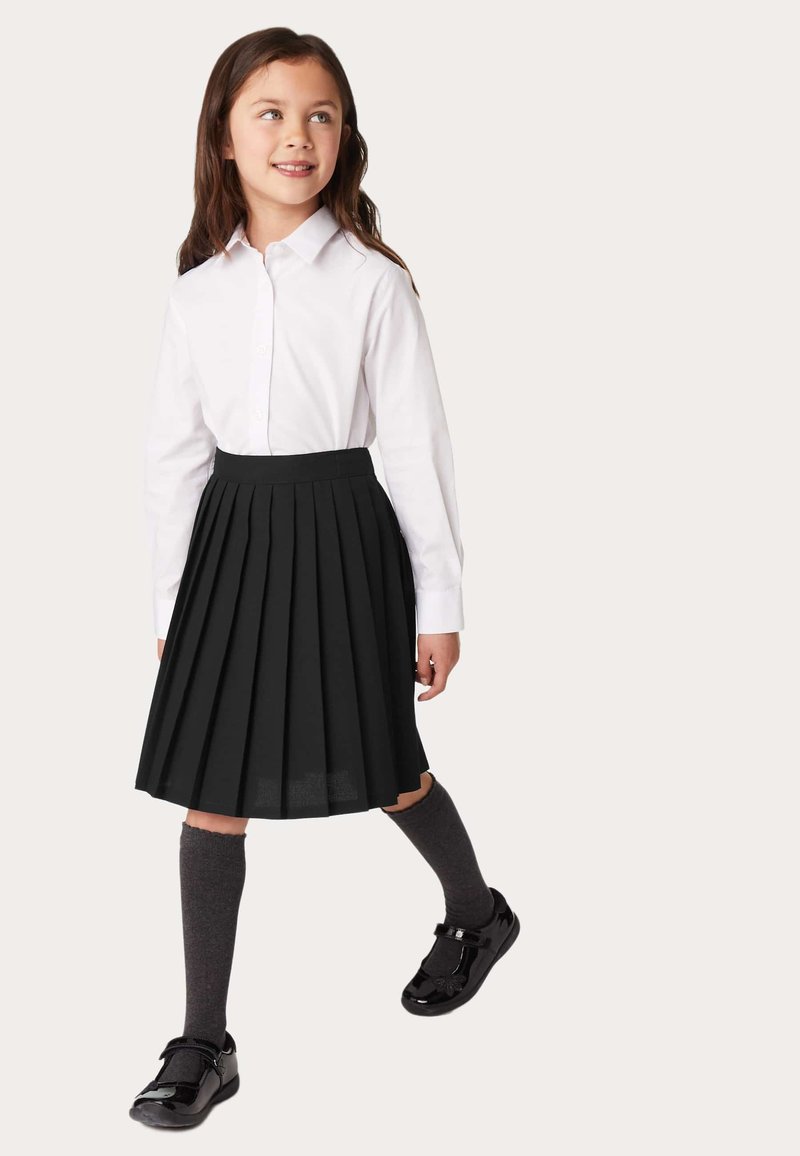 Falda plisada negra, camisa blanca de botones, calcetas grises hasta la rodilla y zapatos de charol negros con una correa. Diseño simple y clásico.