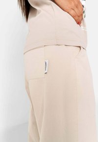 Beige katoenen t-shirt met schoudernauw detail, gecombineerd met beige broek met een achterzak met een label. Glad textuur, casual pasvorm.