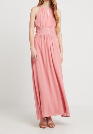 Longue robe rose sans manches avec ceinture en dentelle et encolure en trou de serrure, portée avec des talons nus marron clair.