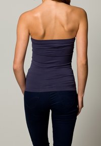 Marinblå strapless topp med rynkad tyg, figurnära siluett och slät textur. Kombinerad med mörkblå jeans med detaljer på bakfickorna.