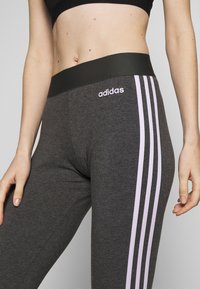 Szare legginsy z czarnym pasem i trzema pionowymi jasnoróżowymi paskami po każdej stronie. Logo Adidas w jasnoróżowym kolorze z przodu.