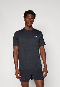 Svart atletisk t-skjorte med korte ermer, har et subtilt mønster, laget av lett stoff, med en logo på brystet.