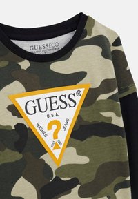 Sweatshirt im Tarnmuster in verschiedenen Grüntönen. Mit einem großen, dreieckigen orangefarbenen Logoaufnäher mit weißem Text und schwarzem, geripptem Halsausschnitt.