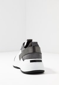 Sneaker in bianco e nero con retro grigio testurizzato, caratterizzati da una robusta fascia nera e una suola bianca zigrinata. Logo sulla suola.