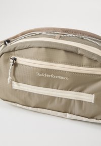 Borsa a tracolla in tessuto beige con finitura testurizzata, caratterizzata da più cerniere, un logo e accenti di webbing orizzontali.
