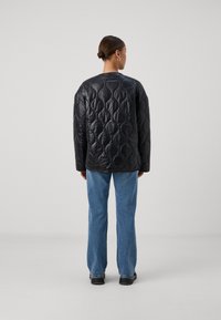 Črna quilted jakna z geometrijskim vzorcem, teksturirano površino, prevelikega kroja, okroglim izrezom, kombinirana s svetloblue jeans hlačami in črnimi čevlji.