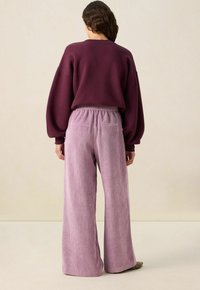 Pantalons en velours côtelé mauve à jambes larges avec une finition texturée et une taille élastique, associés à un sweat-shirt ajusté de couleur bourgogne foncé.