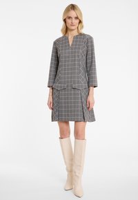 Grijze geruite blouse met een V-hals en driekwart mouwen, gecombineerd met een bijpassende rok,accentueert door crèmekleurige kniehoge laarzen.