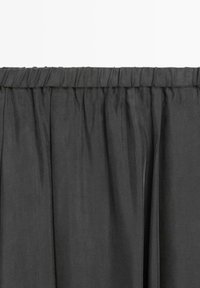 Zwarte stoffen rok met geplooide elastische tailleband en subtiele verticale plooien.