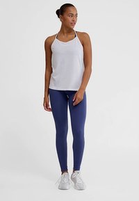 Witte, mouwloze sporttop en marineblauwe geribbelde legging. De top heeft dunne bandjes; de legging is nauwsluitend met een textuur afwerking.