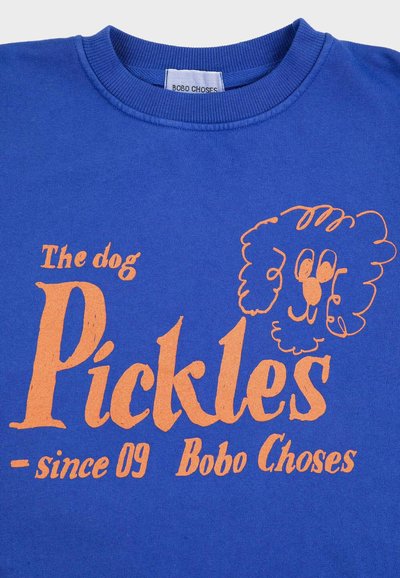 Plava majica s narančastim tekstom "The dog Pickles since 09 Bobo Choses" i jednostavnim linijskim crtežom psećeg lica.