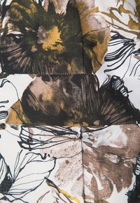Tela floral con grandes flores marrones y verdes sobre un fondo crema, con contornos negros y detalles de superficie texturizados.