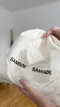 Schnürrbeutel aus weichem, cremefarbenem Stoff; auf zwei Seiten mit dem Schriftzug "SAMSOE" in fettem schwarzen Text bedruckt. Glatte Textur und leicht.