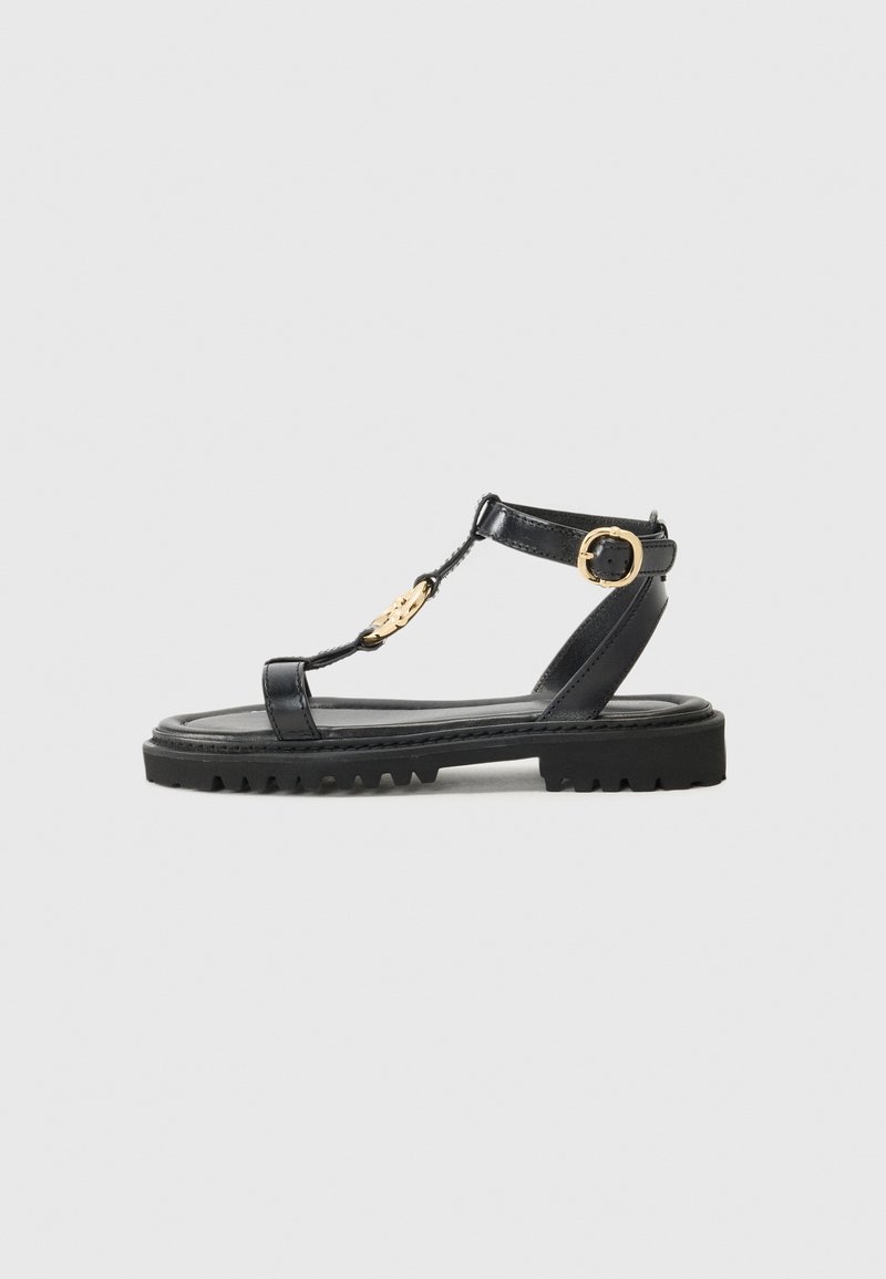 Sandales en cuir noir avec un design à lanière en T, accents en métal doré et une semelle en caoutchouc texturé. Sangle de cheville ajustable pour un meilleur maintien.