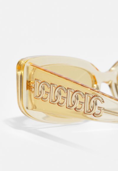 Transparent yellow sunglasses with gold-tone embellishments and a patterned arm featuring intertwined logos. Smooth texture.