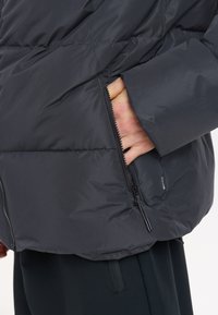 Svart pufferjacka med quiltat mönster och framficka med dragkedja. Slät, glänsande tyg med modern passform och inga synliga mönster eller detaljer.