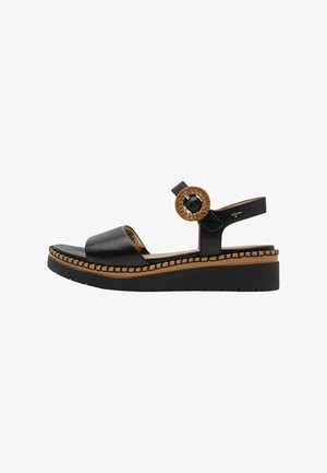 Black leather sandal with wide strap, woven circular accent, and contrasting tan stitching on a chunky black platform sole.