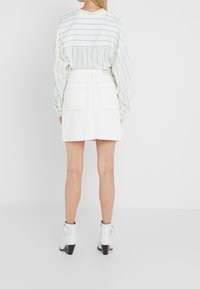 Witte denimrok met twee achterzakken, gecombineerd met een licht gestreept shirt met lange mouwen. Model draagt witte enkellaarsjes met hak.