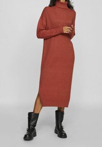 Robe pull col roulé couleur rouille, manches longues, fente latérale, poignets et ourlet côtelés, associée à des bottines en cuir noir.