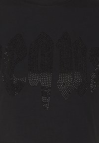 Mustunud T-särk, millel on julge kujundus erineva suurusega rhinestone kiri, mis näitab musta ja hõbeda vahepealset gradienti.