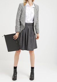Blazer gris texturizado sobre una camisa blanca, combinado con una falda plisada gris. Bolso de mano negro y botas negras hasta el tobillo.