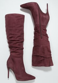 Botas de tacón alto burdeos con una suave textura de ante, con caña hasta la rodilla, diseño holgado y cierre de cremallera en el lado interno.