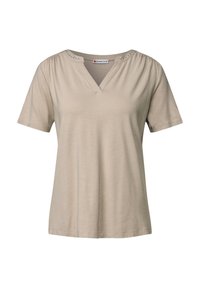 Beige tričko s krátkým rukávem a V-výstřihem, s nabíranými ramínky a dekorativními kovovými hroty kolem výstřihu; vyrobeno z měkké, lehké látky.