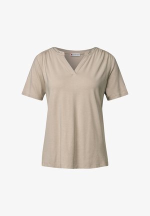 Beżowa koszulka z krótkim rękawem w serek, z zebranymi ramionami i dekoracyjnymi metalowymi ćwiekami wzdłuż dekoltu; wykonana z miękkiego, lekkiego materiału.