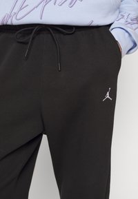 Schwarze Sweatpants aus weichem Stoff mit elastischem Bund und Kordelzug. Mit kleinem weißem Jordan-Logo an der linken Hüfte.