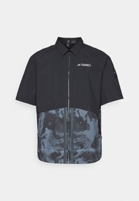 Sort kortærmet skjorte med en frontzipper, der har et blåt abstrakt underpanel og hvid TERREX-logo på brystet.