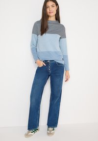 Gestreifter Pullover in Blau- und Schwarztönen, kombiniert mit blauen Jeans mit geradem Bein. Das Outfit wird mit Freizeit-Sneakern mit grünen Akzenten ergänzt.