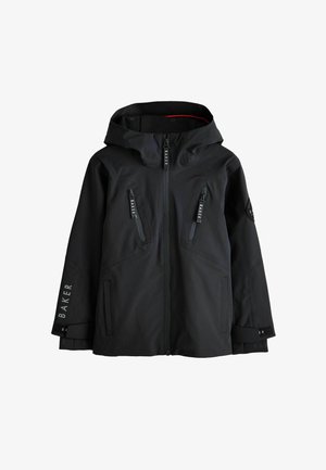 Blonder Junge trägt eine schwarze Kapuzenjacke mit vorderen Reißverschlüssen und dem Wort "Baker" auf Ärmeln und Reißverschlussanhängern.