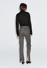 Czarny sweter z golfem w zestawieniu z szarymi spodniami. Spodnie posiadają boczne rozcięcia, dopasowany krój oraz klasyczny wzór w szewron. Na nogach czarne szpilki.