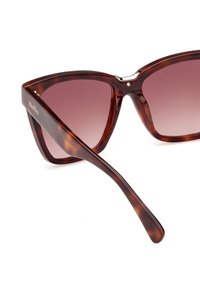 Occhiali da sole tortoiseshell marroni con forma a occhio di gatto, lenti sfumate e dettagli in metallo dorato. Presentano braccia sottili e affusolate e una finitura lucida.